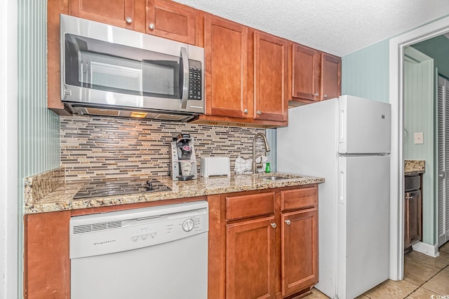 kitchen featuring a textured ceiling, white appliances, a sink, tasteful backsplash, and brown cabinetry