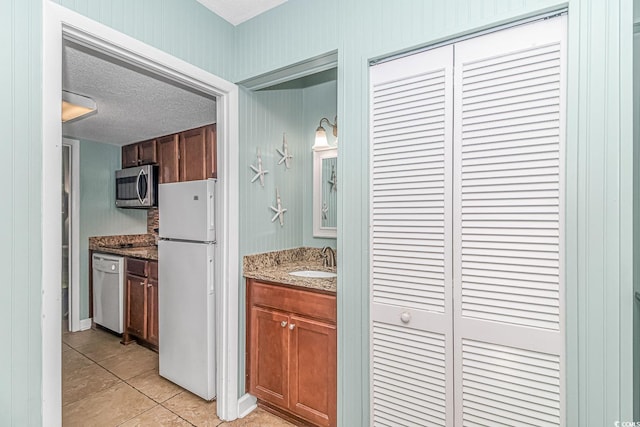 kitchen with dishwashing machine, stainless steel microwave, freestanding refrigerator, a textured ceiling, and a sink