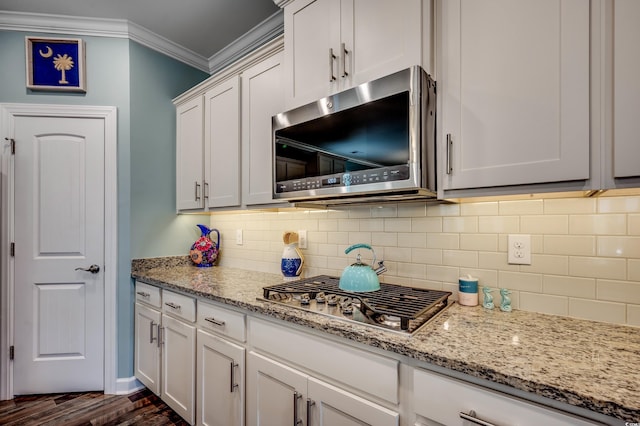 kitchen featuring decorative backsplash, appliances with stainless steel finishes, ornamental molding, dark hardwood / wood-style floors, and white cabinetry