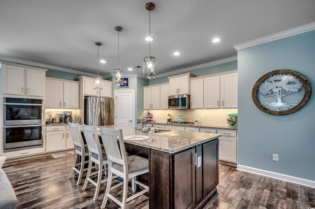 kitchen with appliances with stainless steel finishes, dark wood-type flooring, sink, decorative light fixtures, and a center island with sink