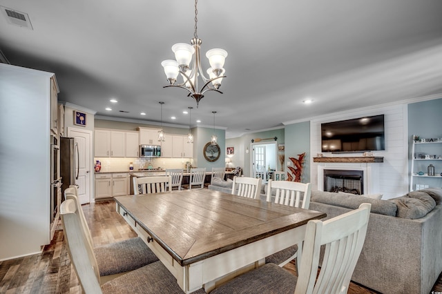 dining space with a large fireplace, wood-type flooring, ornamental molding, and a chandelier