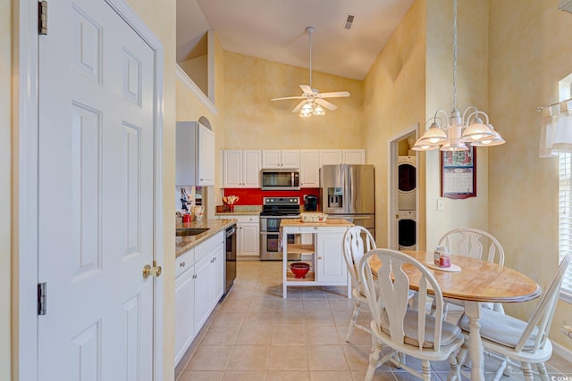 kitchen featuring white cabinets, stainless steel appliances, high vaulted ceiling, and stacked washer / dryer