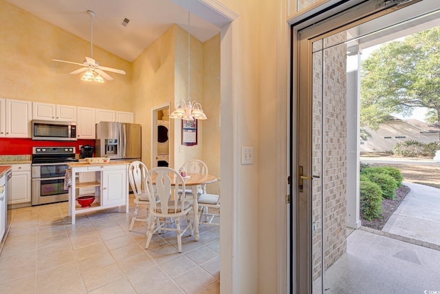 kitchen with appliances with stainless steel finishes, light tile patterned floors, high vaulted ceiling, stacked washer and clothes dryer, and white cabinetry