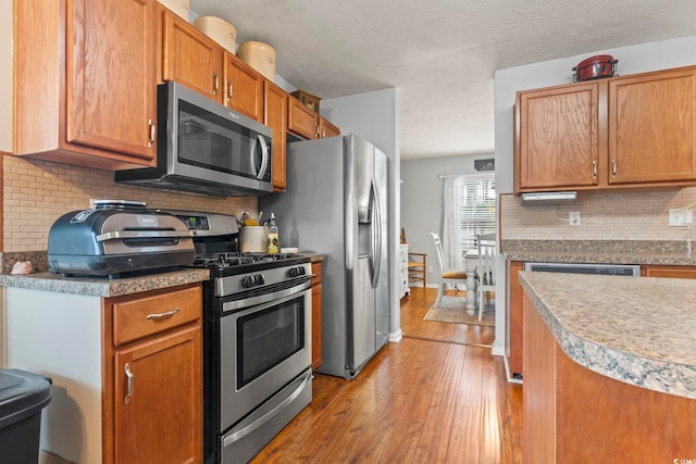 kitchen with appliances with stainless steel finishes, a textured ceiling, light wood-type flooring, and decorative backsplash