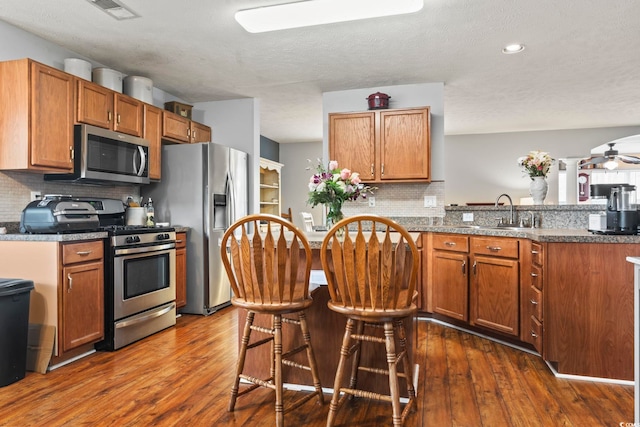 kitchen with appliances with stainless steel finishes, dark hardwood / wood-style flooring, kitchen peninsula, and dark stone countertops