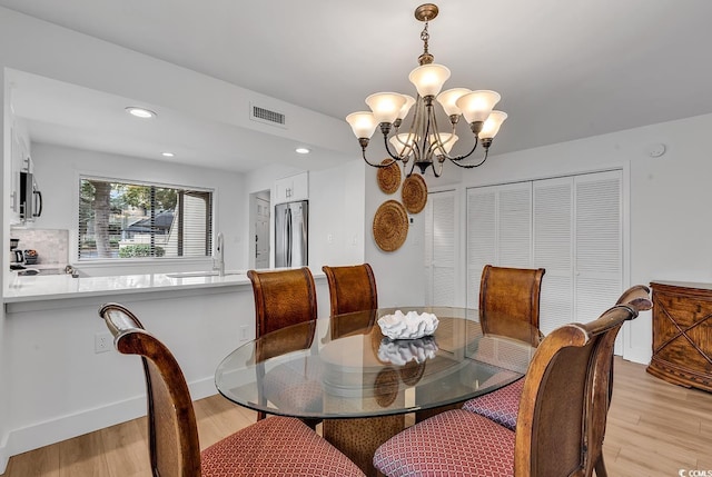 dining space featuring light wood-type flooring, sink, and an inviting chandelier