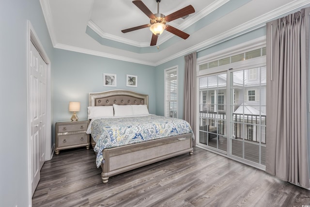 bedroom with crown molding, hardwood / wood-style floors, a tray ceiling, access to outside, and a closet