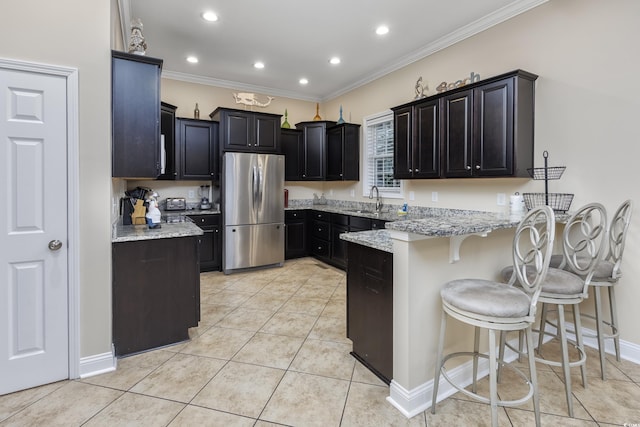 kitchen featuring light tile patterned flooring, stainless steel fridge, light stone countertops, and a breakfast bar area