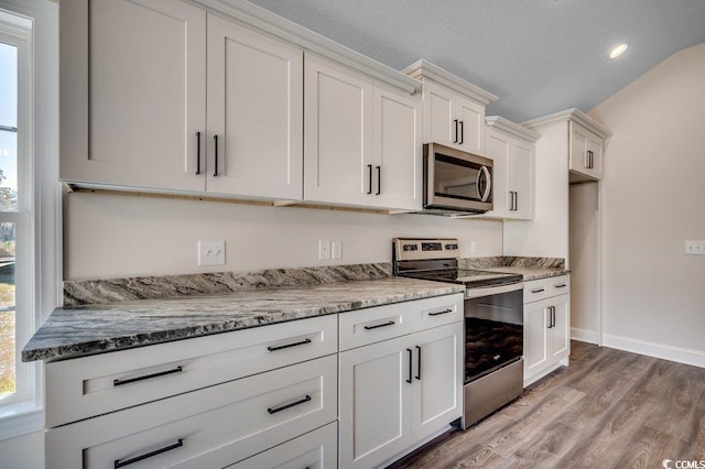 kitchen featuring light stone counters, appliances with stainless steel finishes, a textured ceiling, white cabinets, and hardwood / wood-style flooring