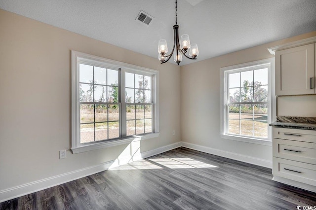 unfurnished dining area with a textured ceiling, dark hardwood / wood-style floors, and a notable chandelier