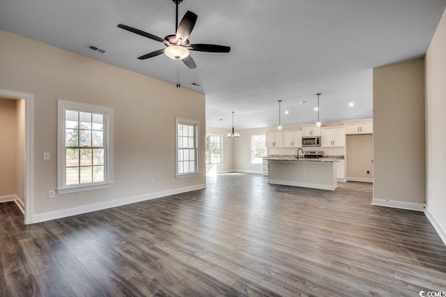 unfurnished living room featuring a textured ceiling, dark wood-type flooring, a healthy amount of sunlight, and ceiling fan with notable chandelier