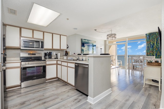 kitchen with white cabinets, expansive windows, light hardwood / wood-style flooring, appliances with stainless steel finishes, and kitchen peninsula