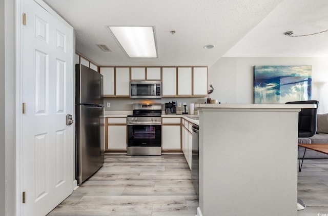 kitchen featuring white cabinetry, light wood-type flooring, a textured ceiling, and appliances with stainless steel finishes