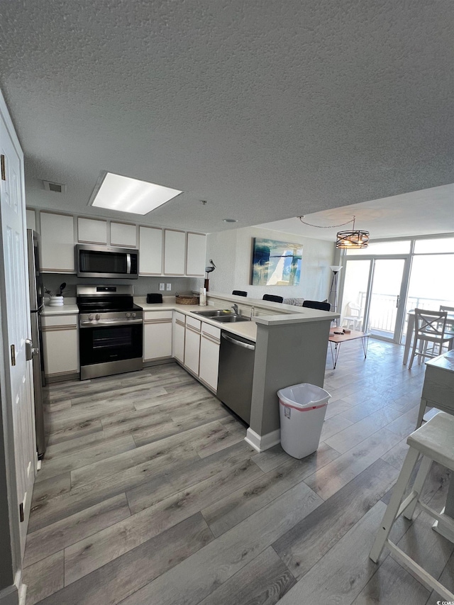 2701 S Ocean Blvd Unit 1808, North Myrtle Beach, SC 29582 - kitchen with stainless steel appliances, a textured ceiling, white cabinetry, light wood-type flooring, and a peninsula