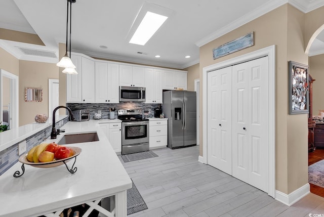 kitchen featuring sink, appliances with stainless steel finishes, decorative light fixtures, white cabinets, and light wood-type flooring