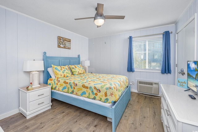 bedroom with ceiling fan, ornamental molding, a wall mounted AC, and light wood-type flooring