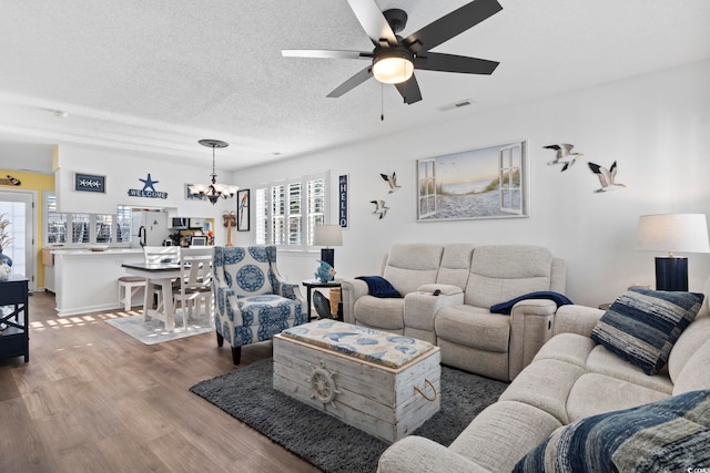 living room with a textured ceiling, wood-type flooring, and ceiling fan with notable chandelier