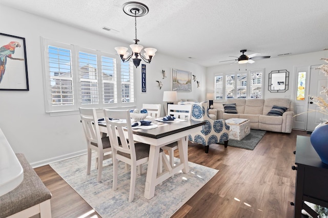 dining area with a textured ceiling, ceiling fan with notable chandelier, a healthy amount of sunlight, and dark wood-type flooring