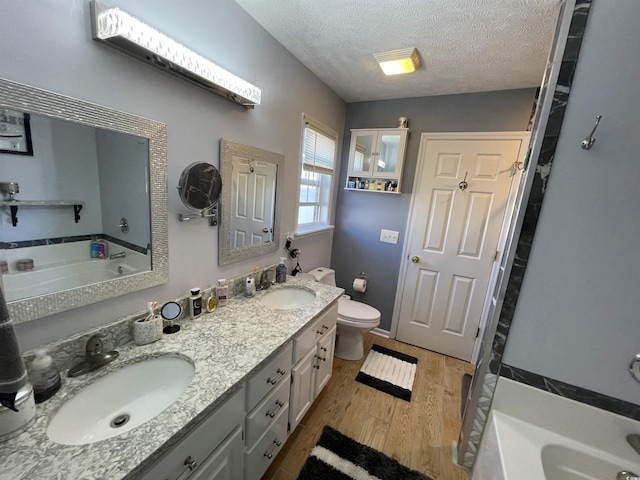 bathroom with a tub to relax in, vanity, a textured ceiling, wood-type flooring, and toilet