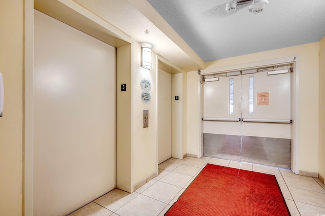 hallway featuring a textured ceiling, elevator, and light tile patterned flooring