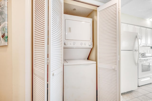 laundry area with stacked washing maching and dryer and light tile patterned floors