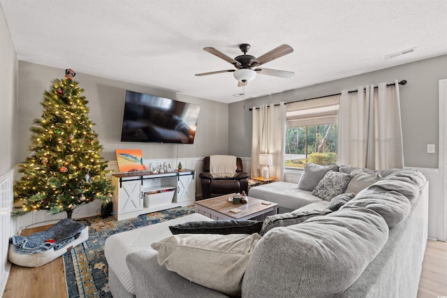 living room with ceiling fan, a textured ceiling, and light hardwood / wood-style flooring