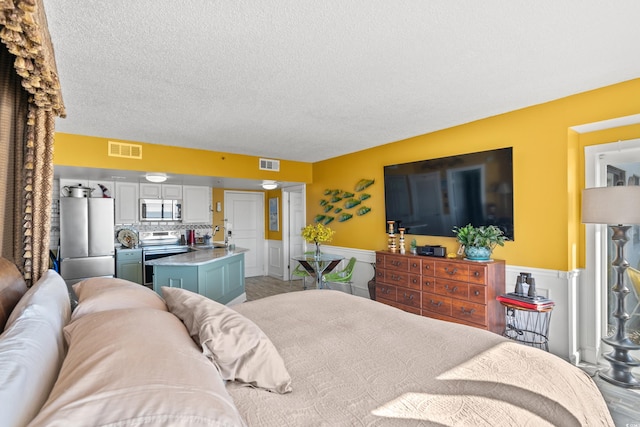 bedroom with stainless steel fridge, sink, and a textured ceiling