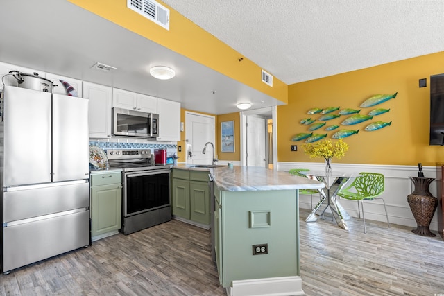 kitchen featuring light hardwood / wood-style flooring, green cabinetry, white cabinetry, kitchen peninsula, and stainless steel appliances