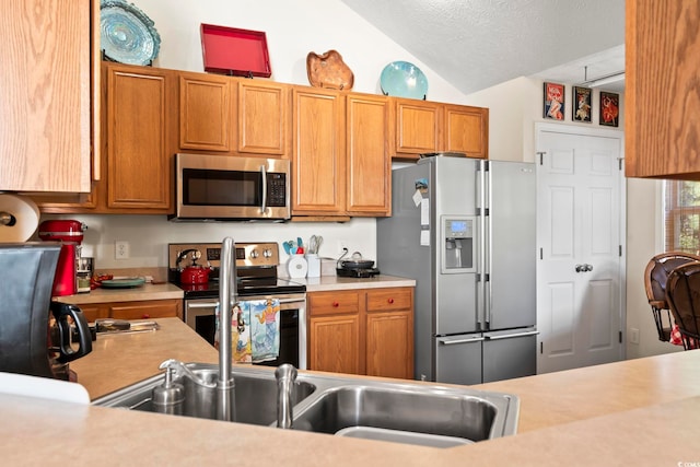 kitchen with a textured ceiling, stainless steel appliances, lofted ceiling, and sink