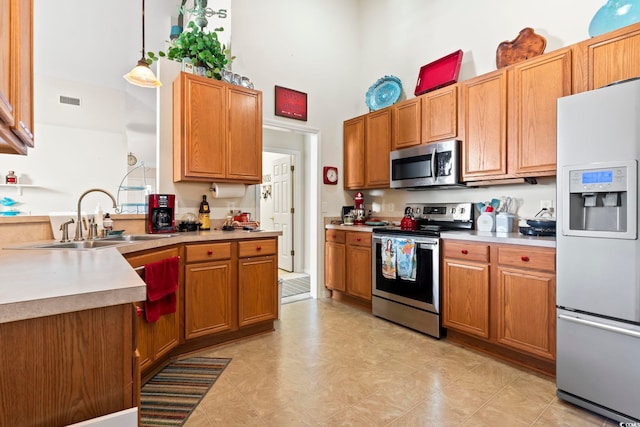 kitchen with decorative light fixtures, sink, stainless steel appliances, and a high ceiling