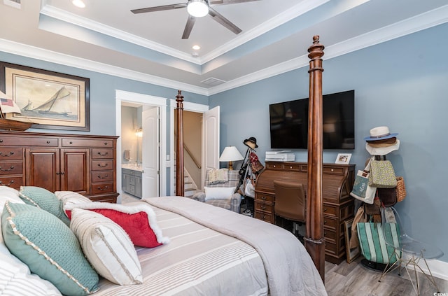 bedroom featuring light wood-type flooring, ornamental molding, a raised ceiling, ceiling fan, and connected bathroom