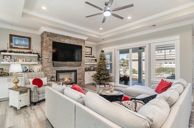 living room with a raised ceiling, crown molding, light hardwood / wood-style flooring, ceiling fan, and a fireplace