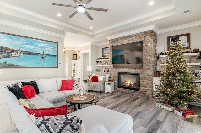 living room featuring a tray ceiling, ceiling fan, crown molding, a fireplace, and hardwood / wood-style floors