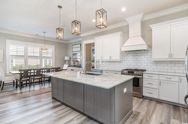 kitchen featuring sink, hanging light fixtures, stainless steel gas range oven, white cabinets, and custom range hood