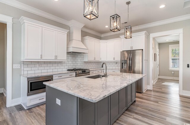 kitchen featuring custom exhaust hood, a kitchen island with sink, sink, pendant lighting, and white cabinets