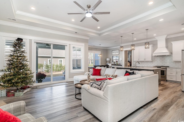 living room with ceiling fan, light hardwood / wood-style floors, a raised ceiling, and crown molding