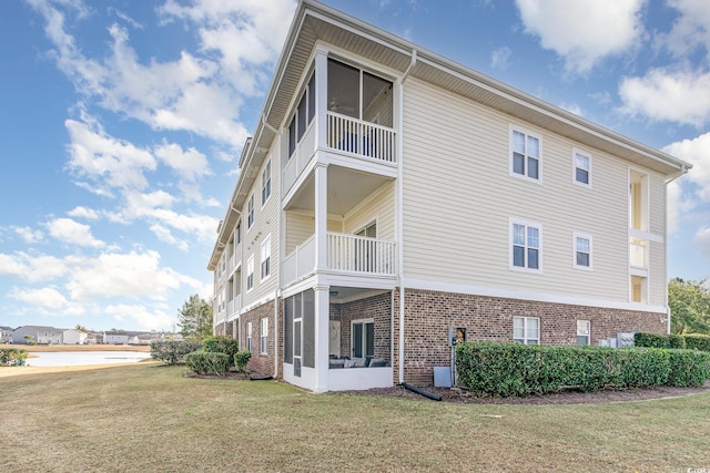 view of side of property featuring brick siding, a lawn, and a balcony