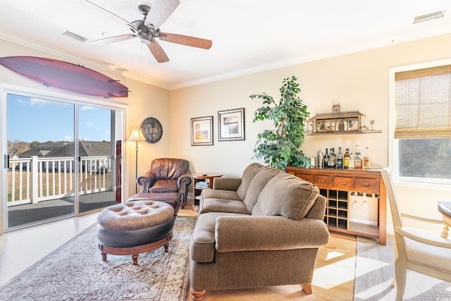 living room with a bar, light wood-type flooring, ceiling fan, and ornamental molding