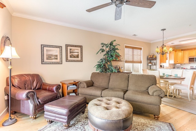 living area with ceiling fan with notable chandelier, light wood-type flooring, and ornamental molding