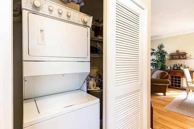 laundry area with wood finished floors, laundry area, stacked washer / drying machine, a textured ceiling, and crown molding