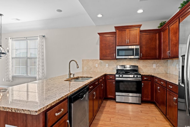 kitchen featuring pendant lighting, sink, light hardwood / wood-style flooring, appliances with stainless steel finishes, and kitchen peninsula