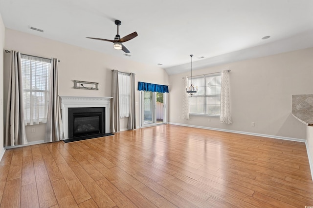 unfurnished living room with ceiling fan with notable chandelier and light wood-type flooring