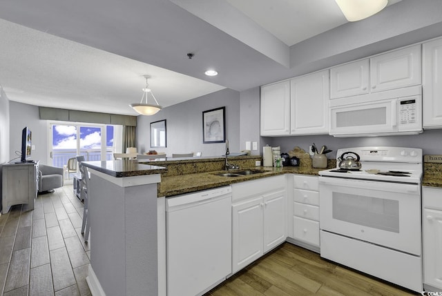 kitchen with white appliances, open floor plan, a peninsula, white cabinetry, and a sink