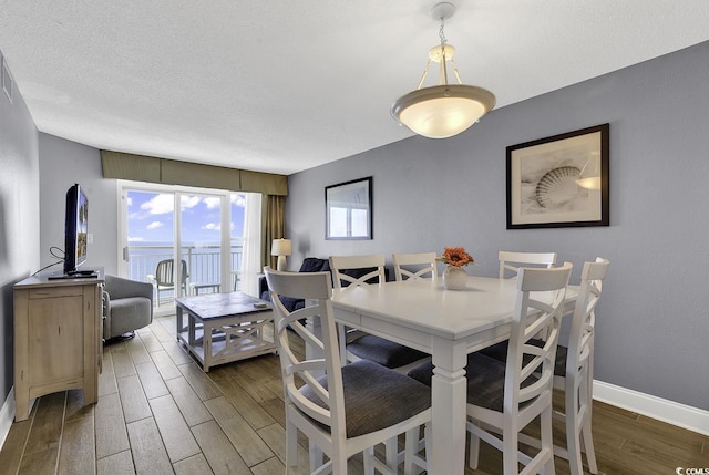 dining area with dark wood-style flooring, a textured ceiling, and baseboards