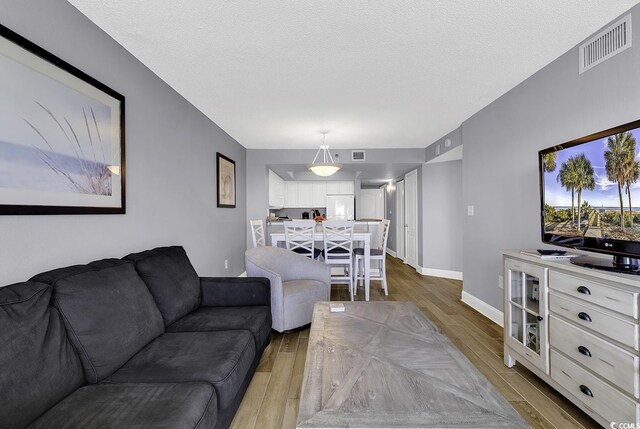 living area featuring visible vents, a textured ceiling, baseboards, and wood finished floors