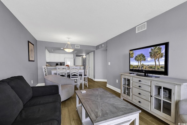 living area with dark wood-style flooring, visible vents, a textured ceiling, and baseboards