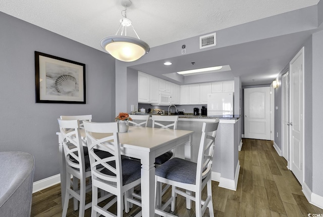 dining area featuring a textured ceiling, dark wood-type flooring, visible vents, and baseboards