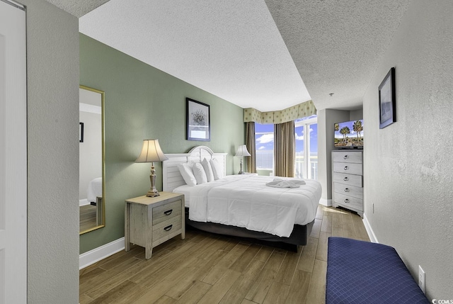 bedroom with a textured ceiling, a textured wall, light wood-type flooring, and baseboards