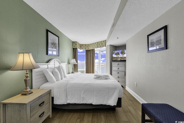 bedroom with a textured wall, wood finished floors, and baseboards