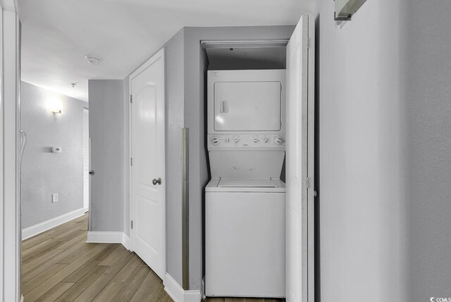 laundry area featuring laundry area, stacked washer and dryer, light wood-style flooring, and baseboards